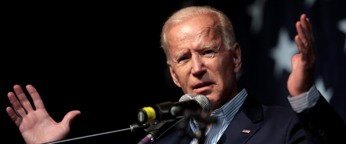 Biden speaks in front of a microphone with his hands outstretched.