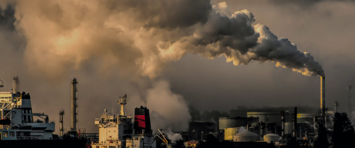 Smokestacks spewing smoke loom over a gray horizon.