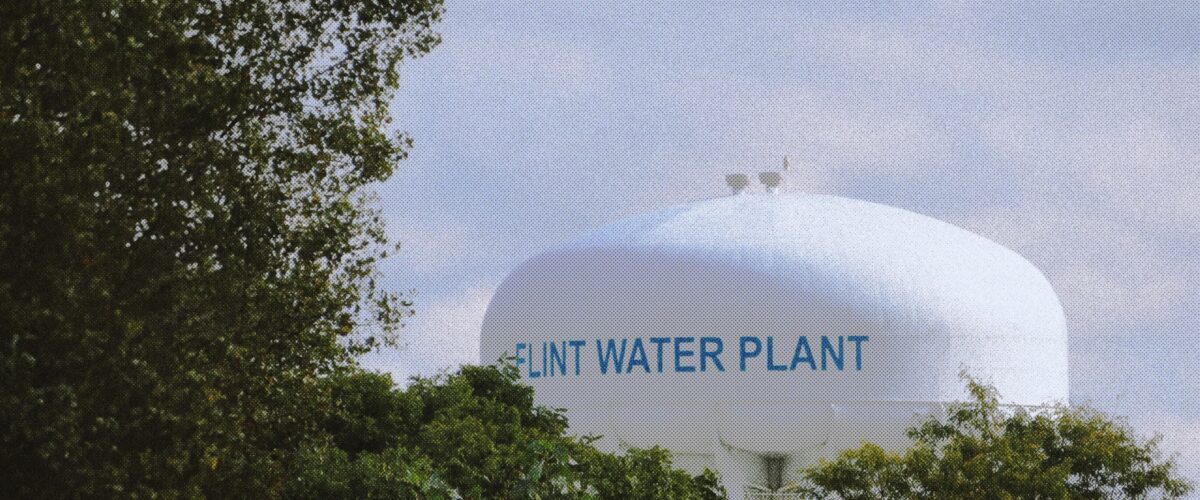 A large round, white water tower labelled "Flint water plant," with green leaves and foliage in front of it.