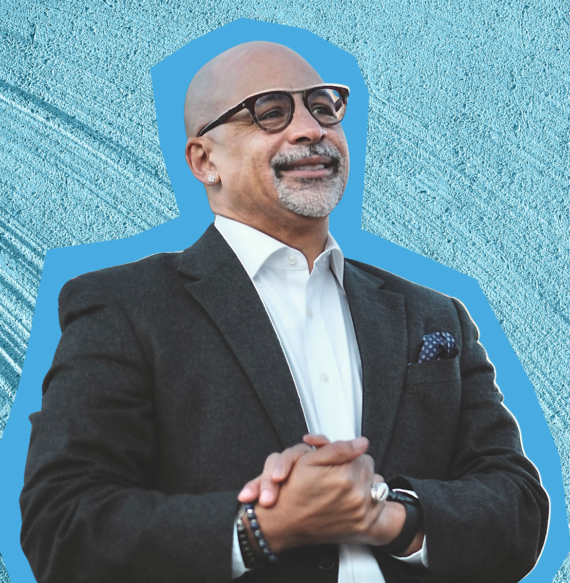 Chris Rabb wears a black suit and smiles, with a blue textured background behind him.